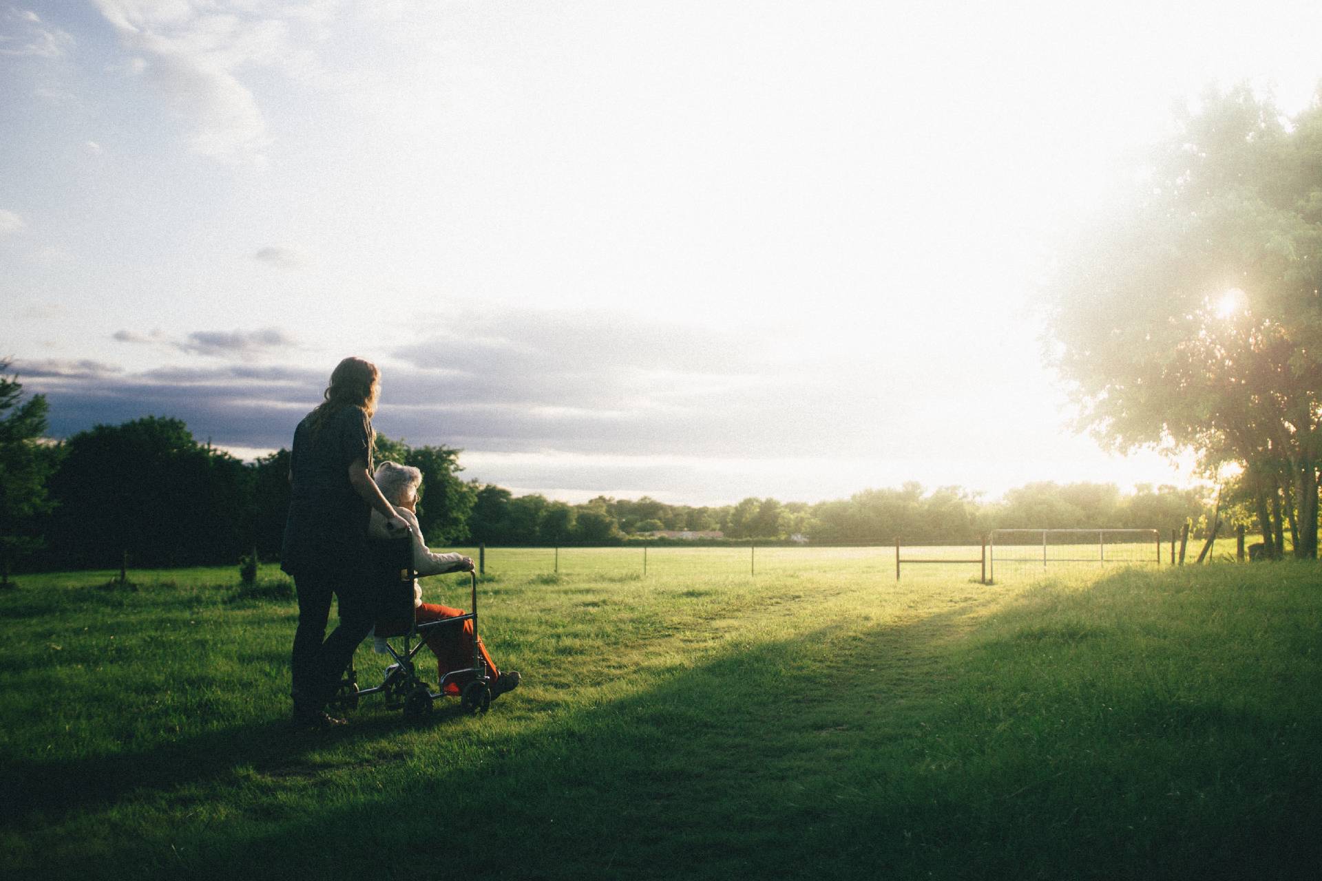 A middle-aged woman standing behind an elderly woman in a wheelchair looking at a sunrise