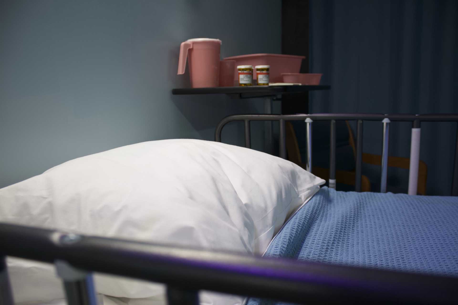 Picture of a hospital bed with bedside table next to it, on which are two boxes of pills
