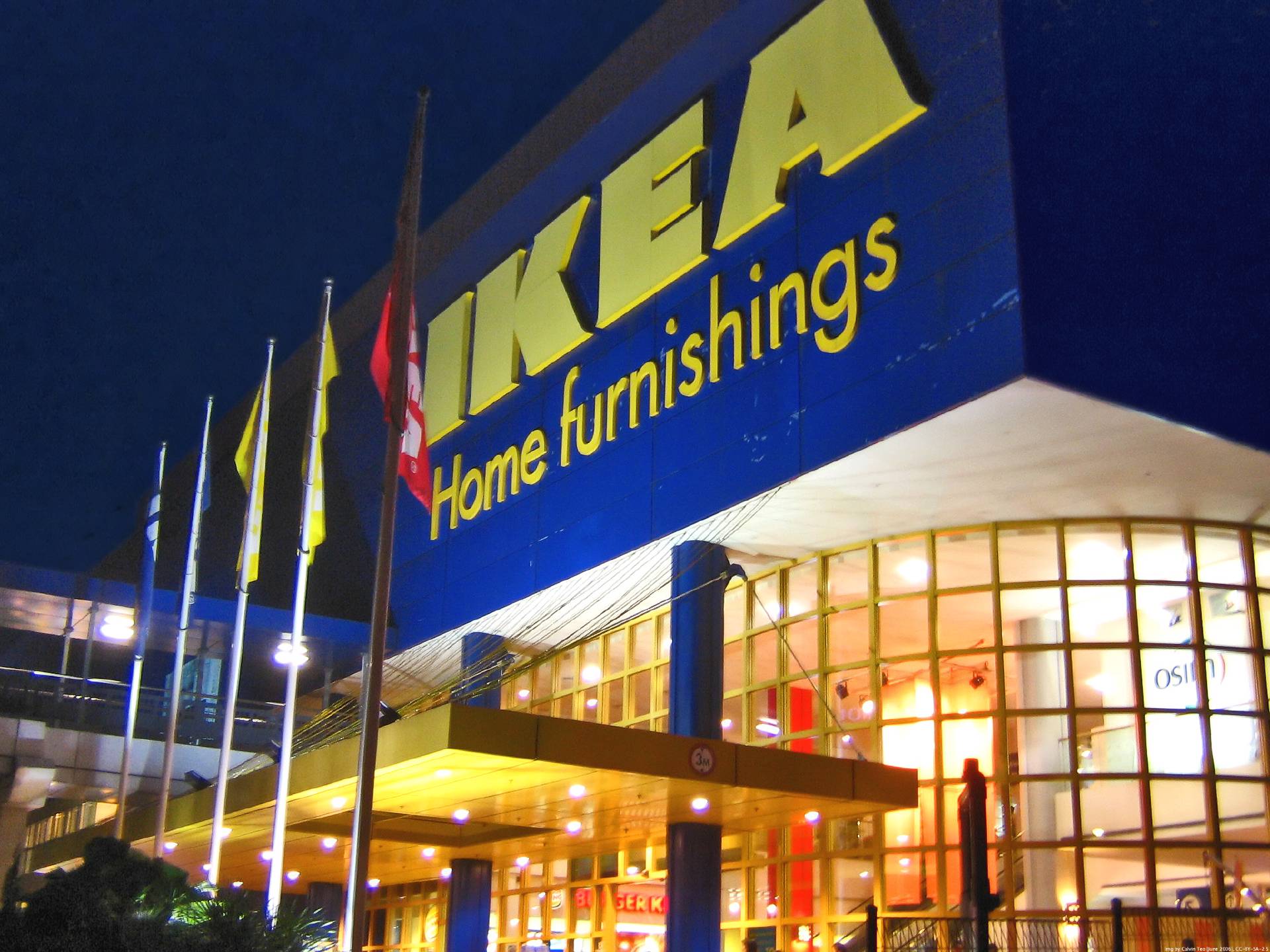 Picture of the store entrance for IKEA, with a series of flags. The building lights are switched on.