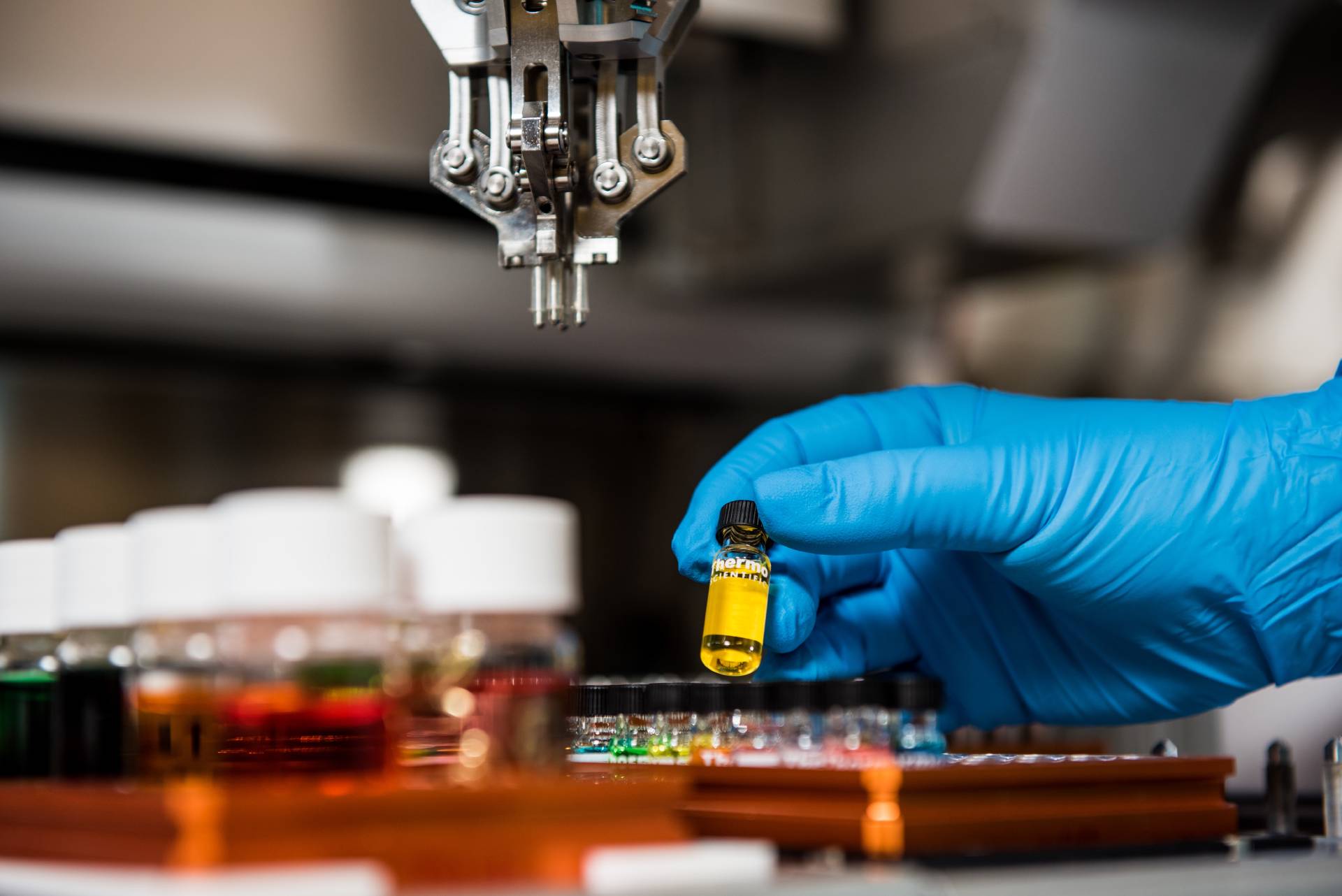 Blue glove holding vial with yellow coloured liquid, above a tray full of vials.