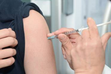 Picture of a woman with sleeve rolled up and a man holding a syringe administering a vaccination